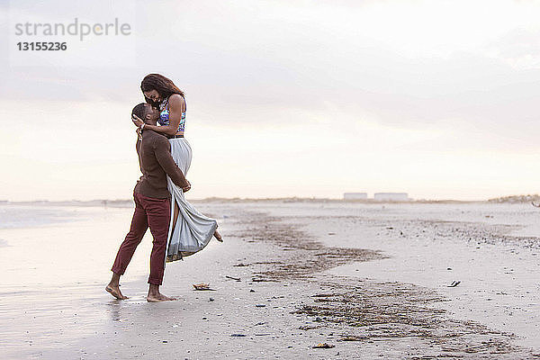 Paar am Strand  Umarmung  von Angesicht zu Angesicht  Mann hebt Frau hoch