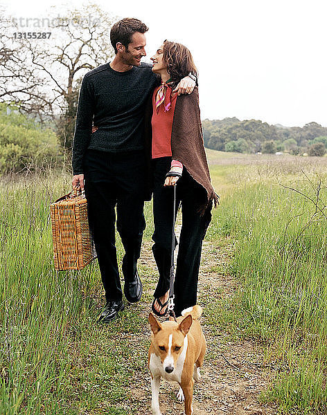 Ehepaar geht mit Hund in der Natur spazieren  mit Picknickkorb