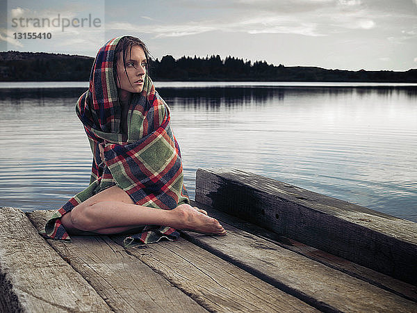 Frau in Decke auf Steg am See