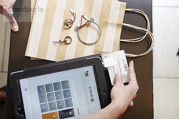 Ältere Frau benutzt ein digitales Tablet  um die Kreditkarte eines Kunden in einer Modeboutique aufzuladen  Fokus auf die Hände  Draufsicht