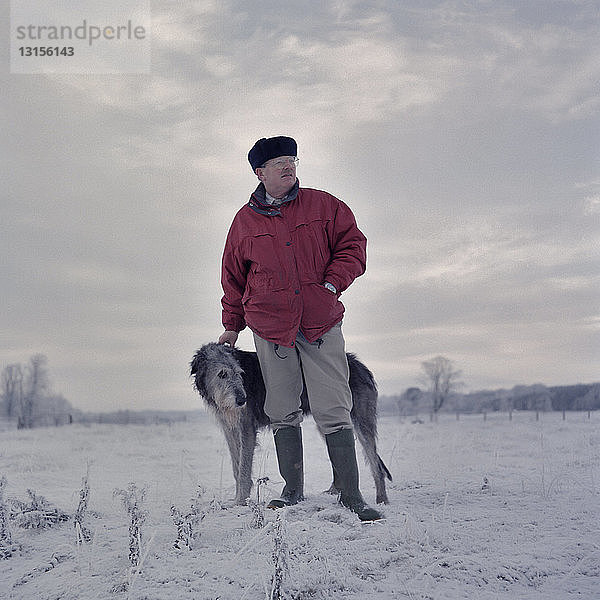 Porträt eines Mannes mit Hirschhund in einem verschneiten Feld