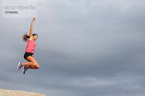 Frau springt vor Freude auf Felsbrocken