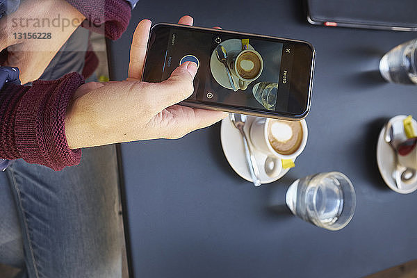 Draufsicht auf eine mittelgroße erwachsene Frau  die mit ihrem Smartphone in einem Straßencafé einen Tisch fotografiert