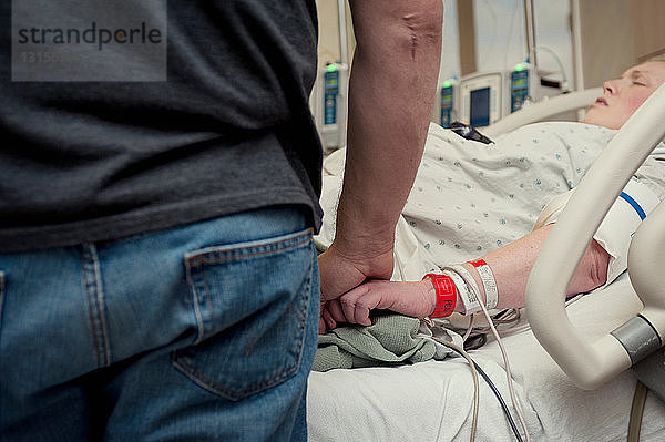 Mann hält die Hand einer Frau im Krankenhauszimmer
