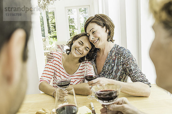 Vier erwachsene Freunde trinken gemeinsam Rotwein am Esstisch