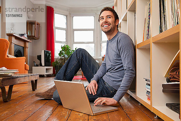 Junger Mann sitzt auf Holzboden und benutzt einen Laptop
