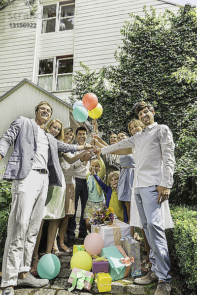 Porträt einer Drei-Generationen-Familie  die Geburtstagsballons im Garten hochhält