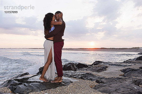 Paar steht auf Felsen am Meer  umarmt sich  von Angesicht zu Angesicht