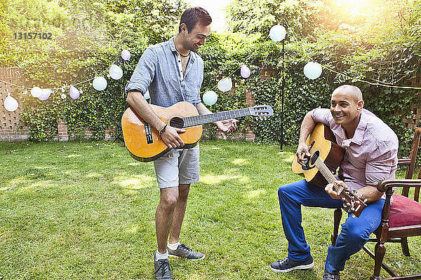 Zwei männliche Freunde spielen akustische Gitarre im Garten