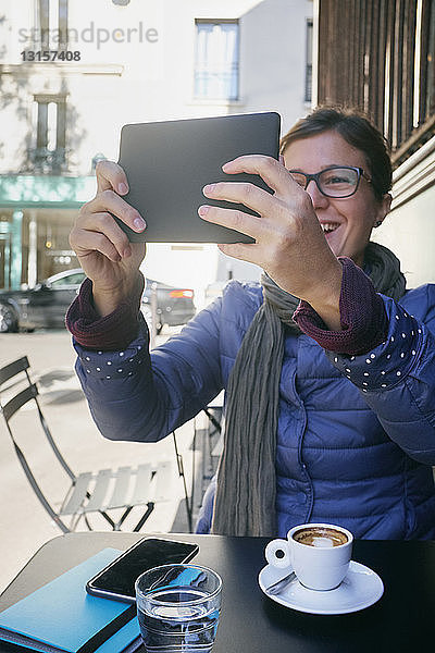 Mittlere erwachsene Frau  die in einem Straßencafé ein digitales Tablet-Selfie macht