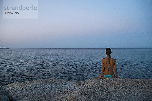 Junge Frau sitzt auf einem Felsen und schaut aufs Meer hinaus  Costa rei  Sardinien  Italien
