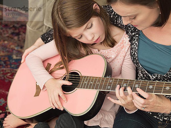 Mittlere erwachsene Frau bringt ihrer Tochter das Gitarrenspiel bei