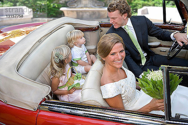 Hochzeitspaar mit Kindern im Auto