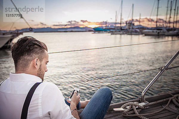 Junger Mann benutzt Smartphone auf Yacht  Cagliari  Sardinien  Italien