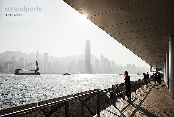 Silhouettierte Seitenansicht einer jungen Frau  die über das Wasser auf die Skyline schaut  Hongkong  China