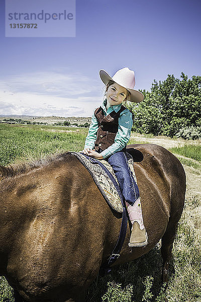 Mädchen mit Cowboystiefeln und Hut auf einem Pferd
