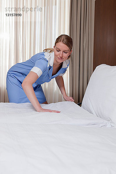 Zimmermädchen macht ein Bett im Hotelzimmer