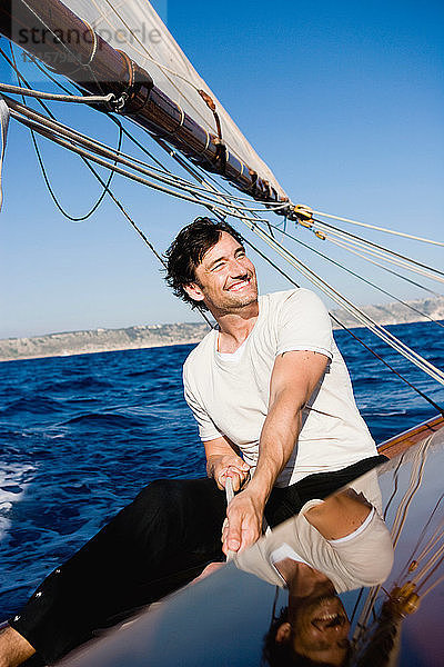 Mann lächelnd am Steuer eines Segelboots