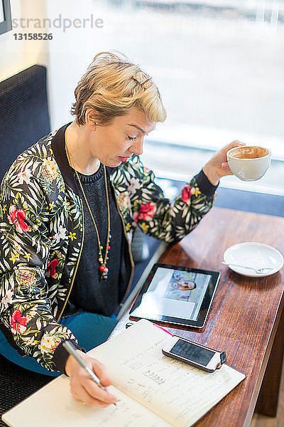 Frau führt Videogespräch und schreibt in einem Café in einen Notizblock