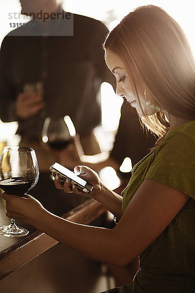 Geschäftsfrau schaut in einer Weinstube auf ihr Handy