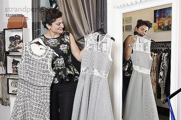 Reife Frau in Modeboutique  hält zwei verschiedene Kleider
