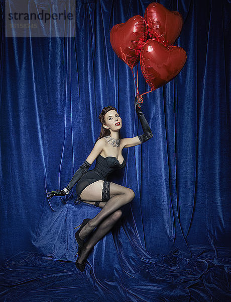 Burlesque-Tänzerin hält rote herzförmige Luftballons