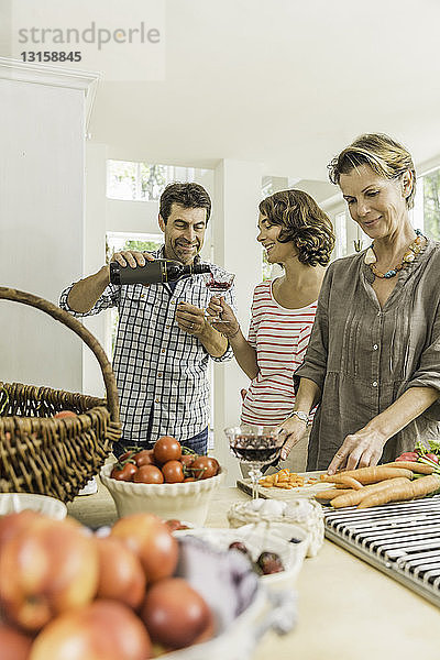Drei Erwachsene schenken Rotwein ein  während sie frisches Gemüse zubereiten