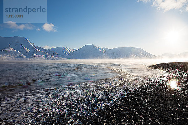 Blick auf die sonnenbeschienene Küste und die fernen Berge  Svalbard  Norwegen
