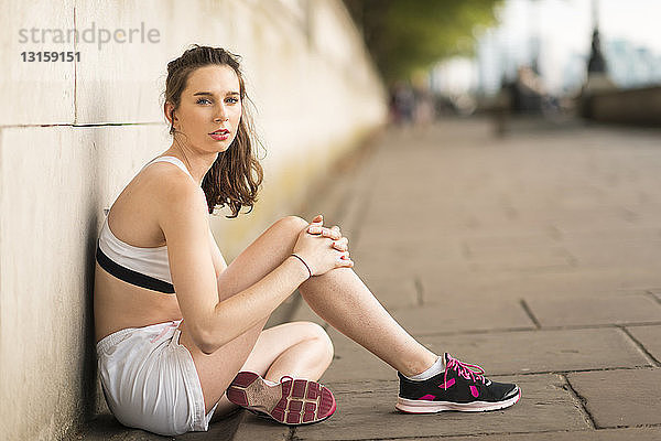 Porträt einer jungen Läuferin am Flussufer sitzend