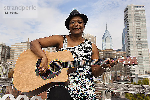 Porträt einer glücklichen reifen Frau beim Gitarrenspiel vor der Skyline von Philadelphia  USA