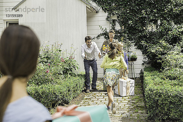 Älteres Paar mit offenen Armen  das die Familie im Garten begrüßt