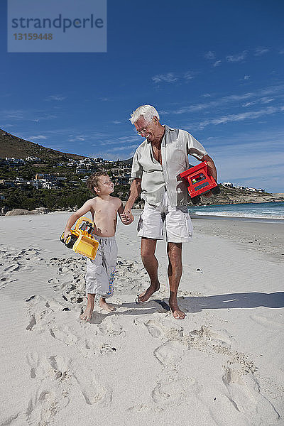 Mann hält die Hand seines Enkels am Strand