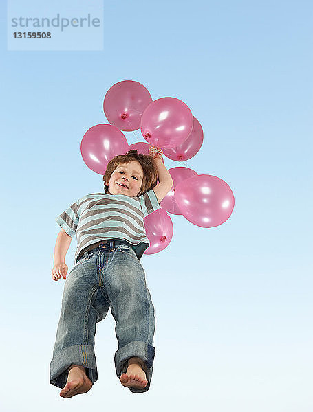 Junge springt mit einem Bündel Luftballons
