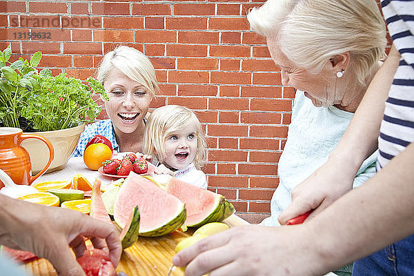 Vier Frauen und ein weibliches Kleinkind bereiten das Essen am Gartentisch vor