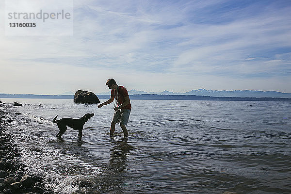 Mann spielt mit seinem Hund am Ufer des Puget Sound  Seattle  Washington State  USA