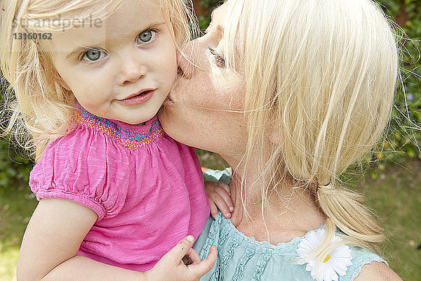 Nahaufnahme einer jungen erwachsenen Mutter  die ihre kleine Tochter im Garten küsst
