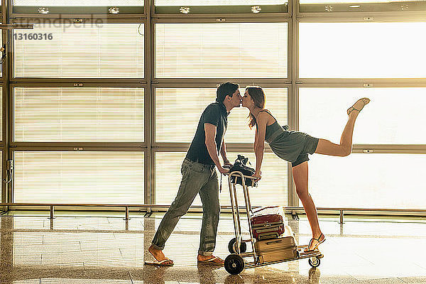 Junges Paar mit Gepäckwagen küsst sich im Flughafen