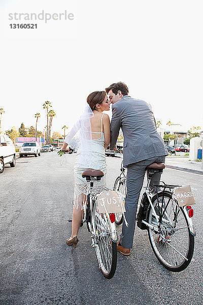 Junges frisch verheiratetes Paar küsst sich auf Fahrrädern auf der Straße