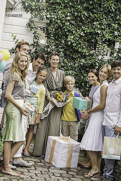 Porträt einer dreiköpfigen Familie im Garten mit Blumenstrauß und Geburtstagsgeschenken