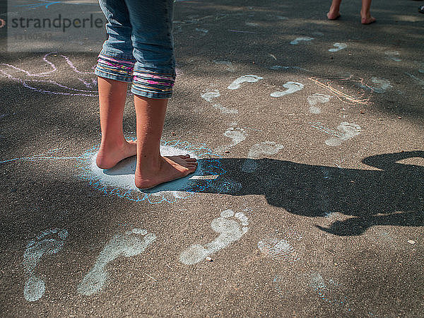 Nackte Füße eines Mädchens machen Kreide Fußabdrücke auf dem Bürgersteig