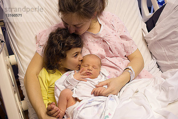 Mutter hält neugeborenes Baby mit Tochter im Krankenhausbett