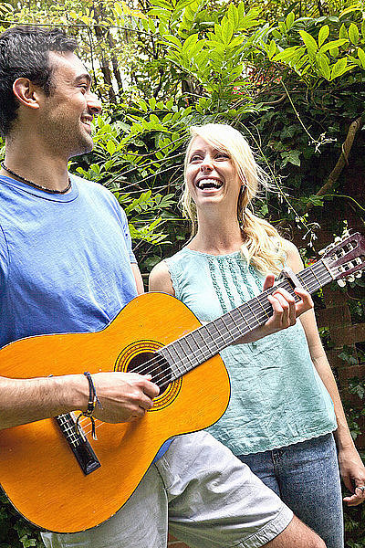 Junger Mann spielt Akustikgitarre im Garten für seine Freundin