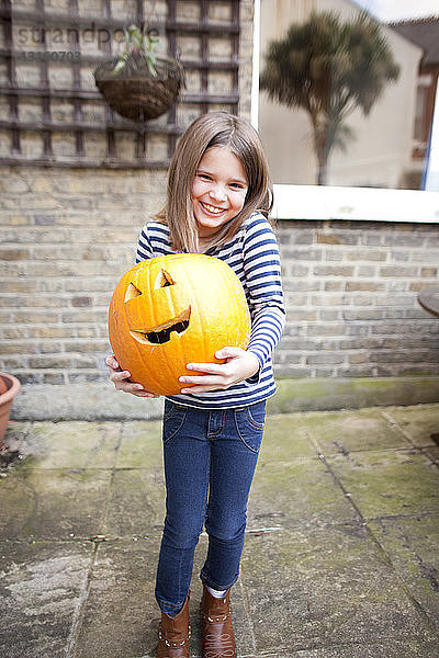 Lächelndes Mädchen hält schweren Halloween-Kürbis im Garten