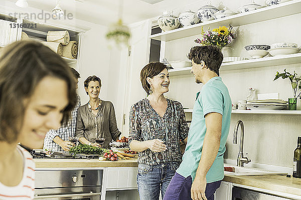 Fünf erwachsene Freunde unterhalten sich und bereiten Essen in der Küche zu
