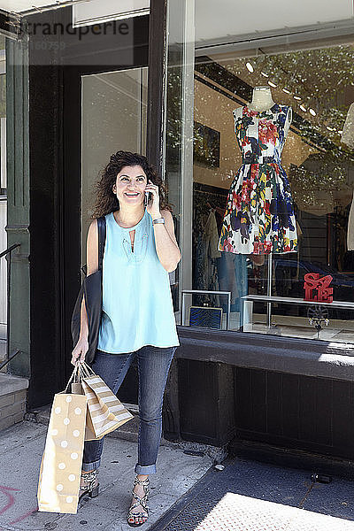 Ältere Frau verlässt eine Modeboutique mit Einkaufstaschen und Smartphone