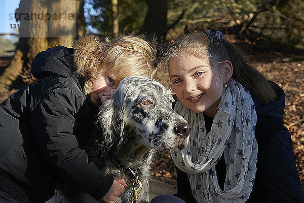 Junger Bruder und junge Schwester umarmen Hund  im Freien