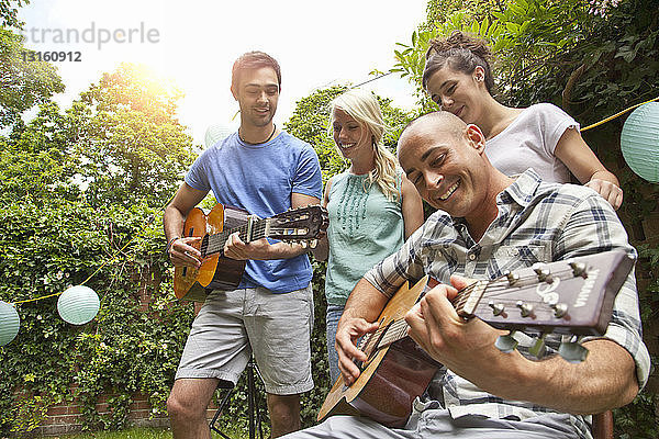 Männliche Freunde spielen akustische Gitarre im Garten für Freundinnen