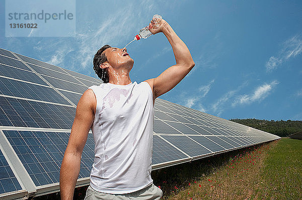 Mann trinkt vor einem Sonnenkollektor