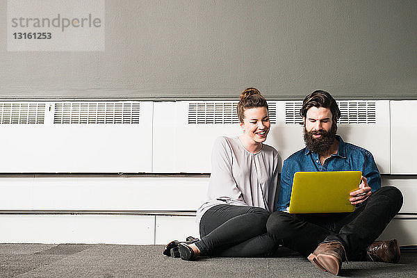 Junger Mann und Frau sitzen auf dem Boden und benutzen einen Laptop