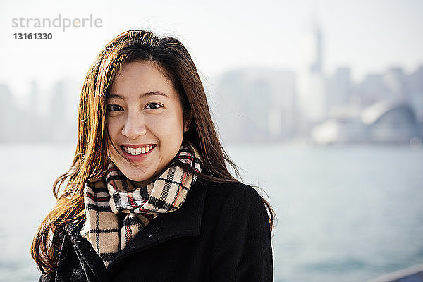 Porträt einer jungen Frau mit kariertem Schal vor einem Wasser  die lächelnd in die Kamera schaut